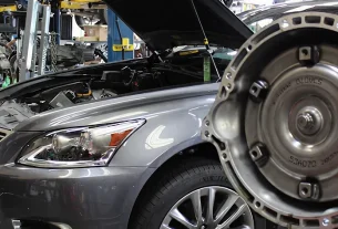 Close-up of a car in an automotive shop with the hood open, showcasing mechanical components and repair tools.