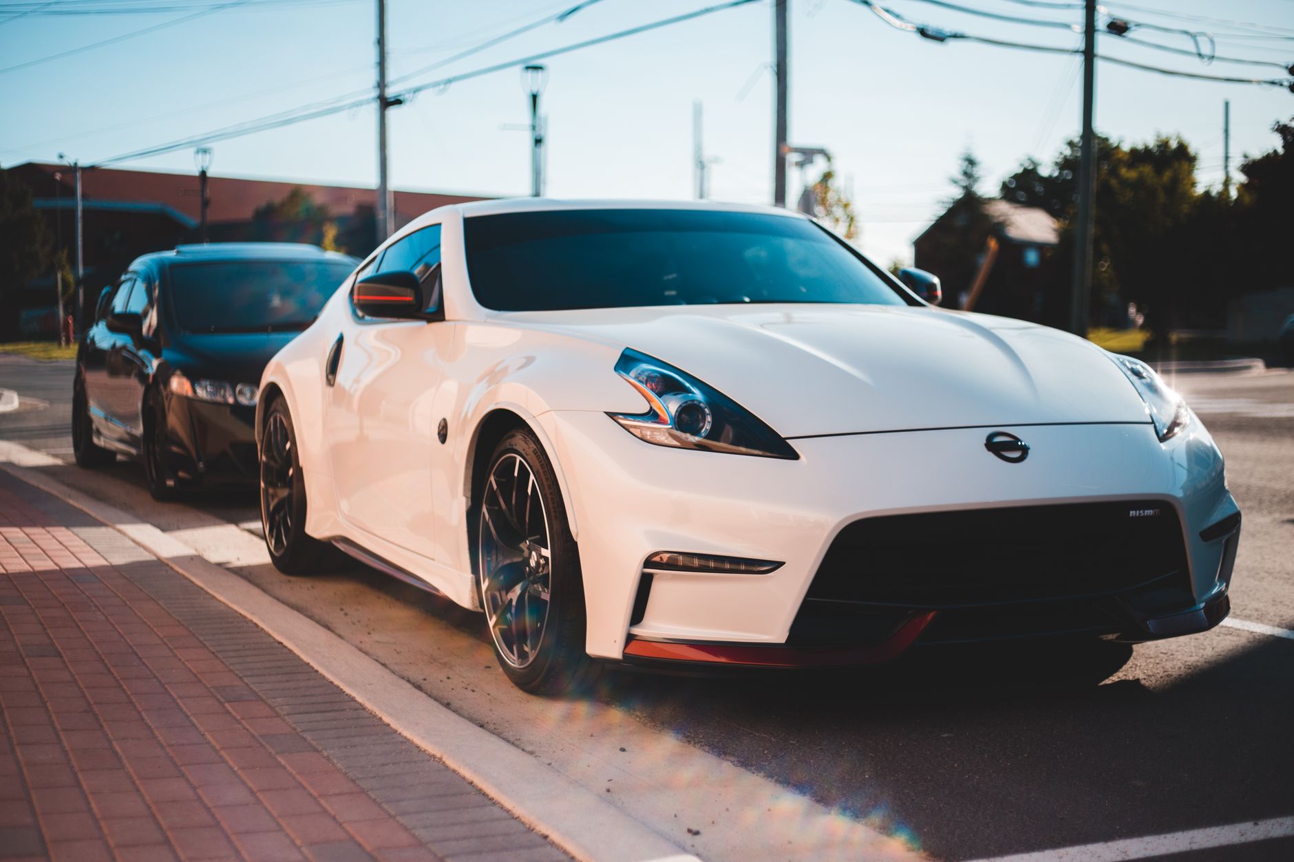 White tuned sports cars parked on asphalt road under wires and blue cloudless sky in settlement on blurred background — 2020
