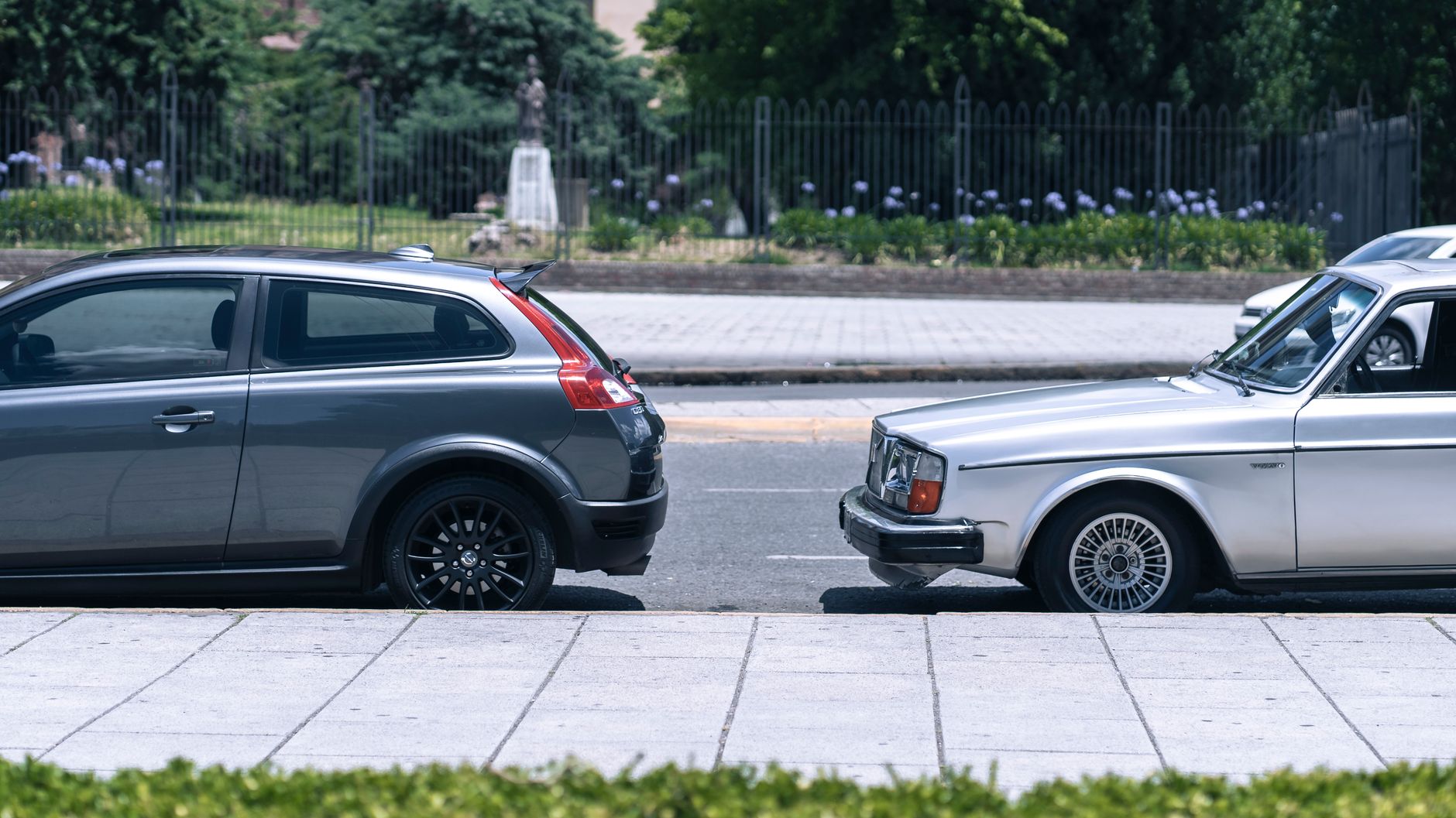 A close-up view of two cars parked on a city street near a green park on a sunny day. — 6 things you should know about Kia Se