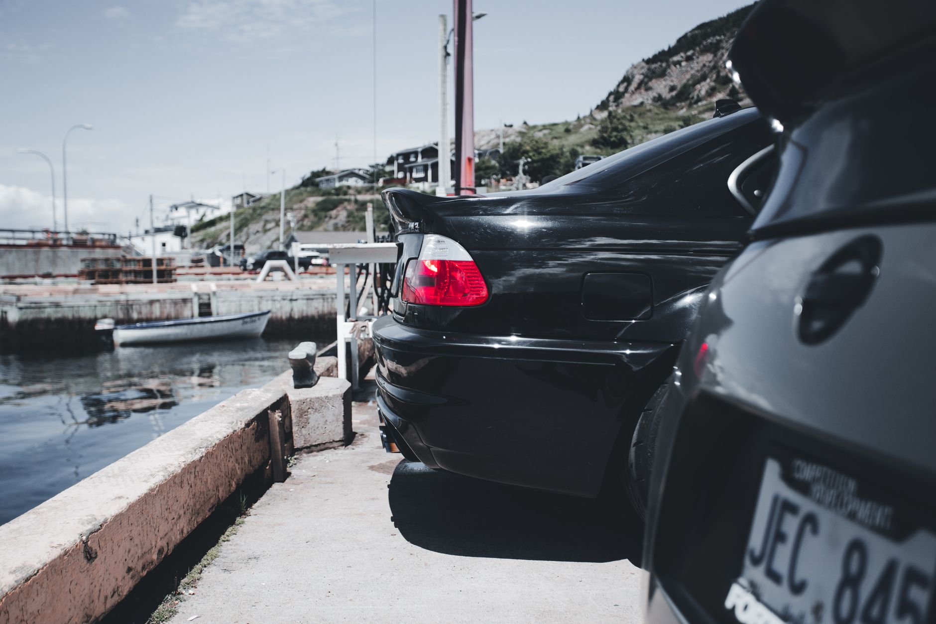 Close-up of classic black cars parked by a peaceful waterfront harbor on a sunny day. — Add Style With Mustang Accessories