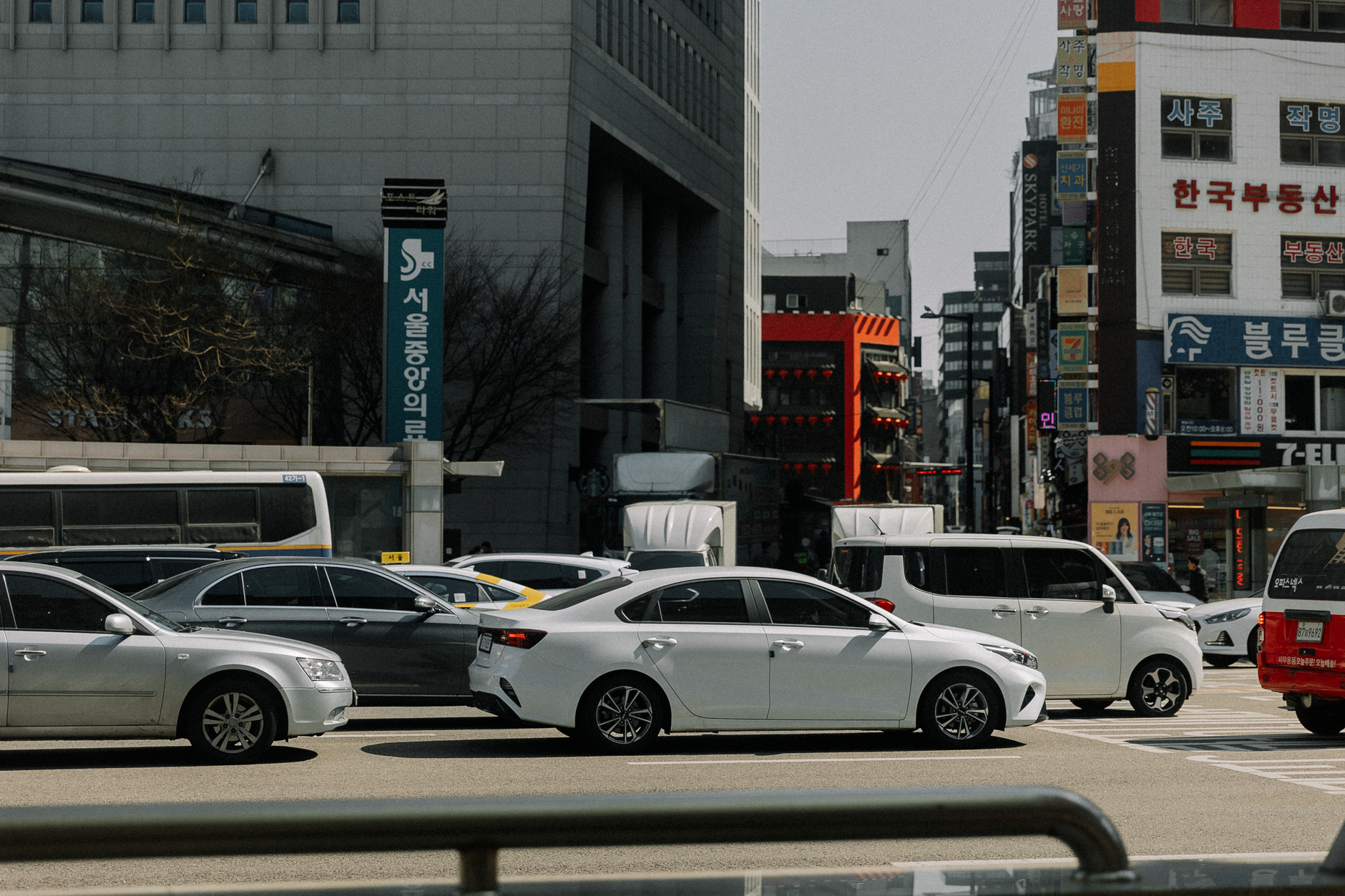 A busy urban intersection with cars and modern buildings on a sunny day. — Automotive Advertising Agencies Concentrate on Peo