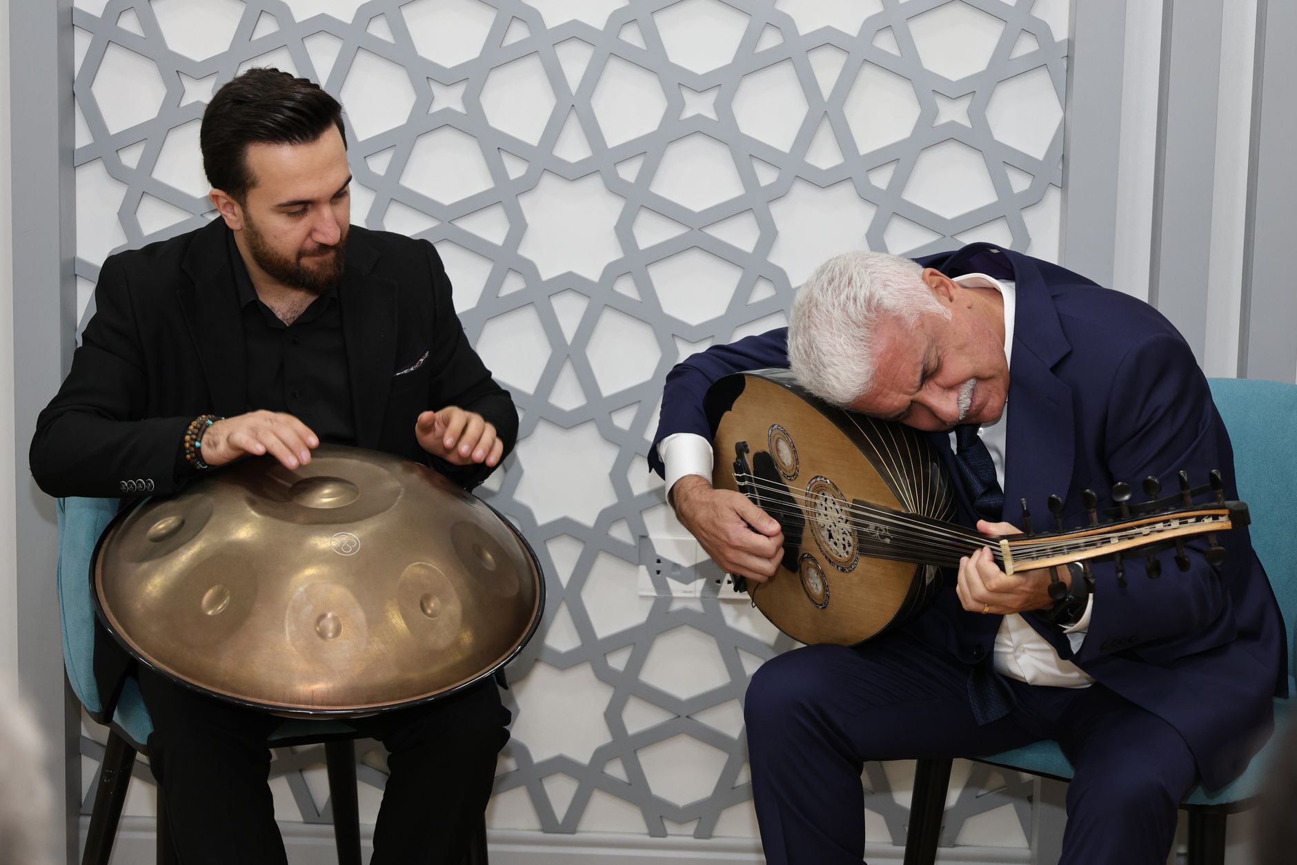 Two musicians playing oud and handpan in a cozy indoor setting, conveying cultural richness and musical harmony. — Get Guidel