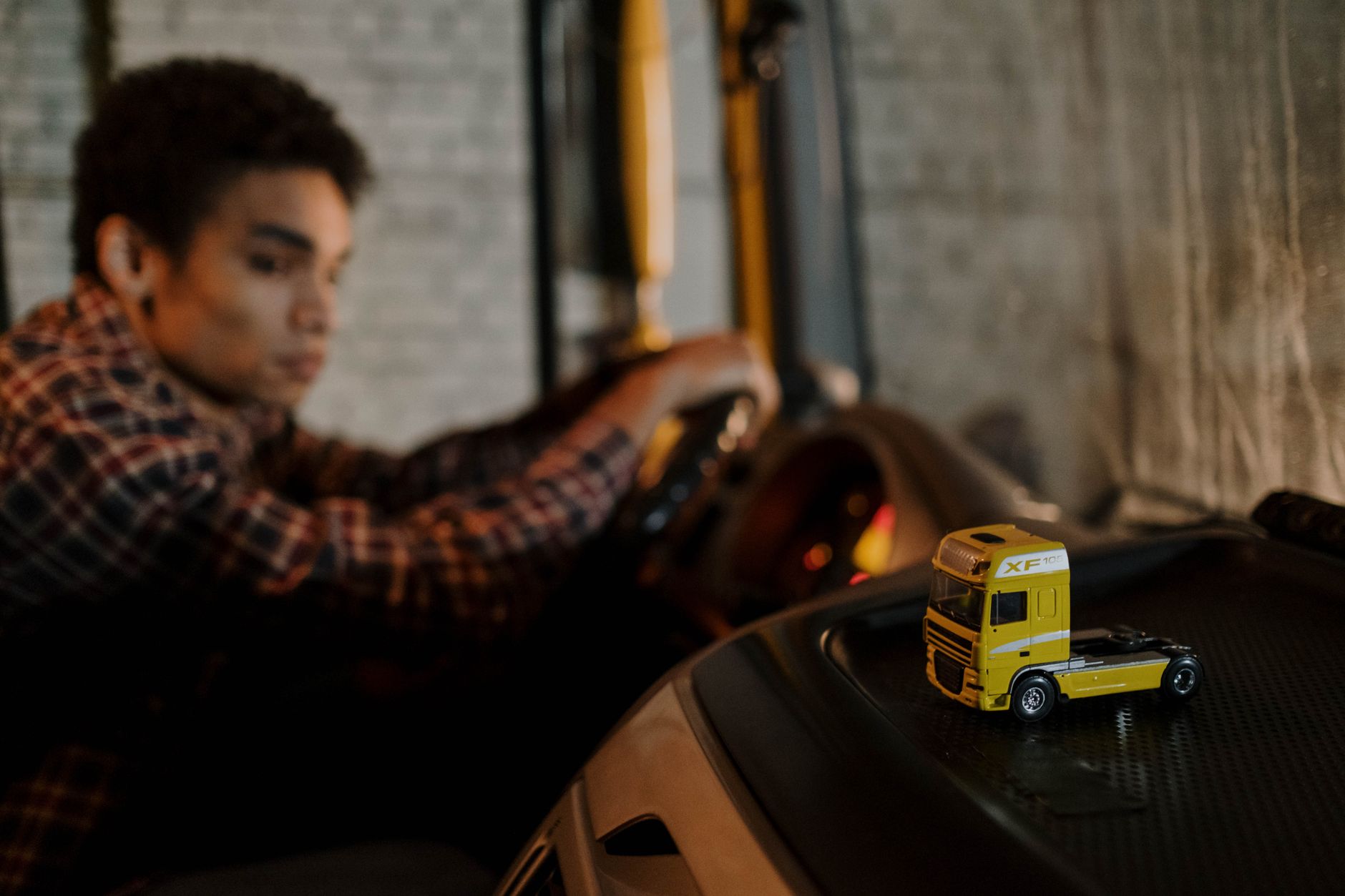 A driver in a truck cab with a focus on a miniature yellow truck toy, creating a blurred background. — GMC Trucks - a century