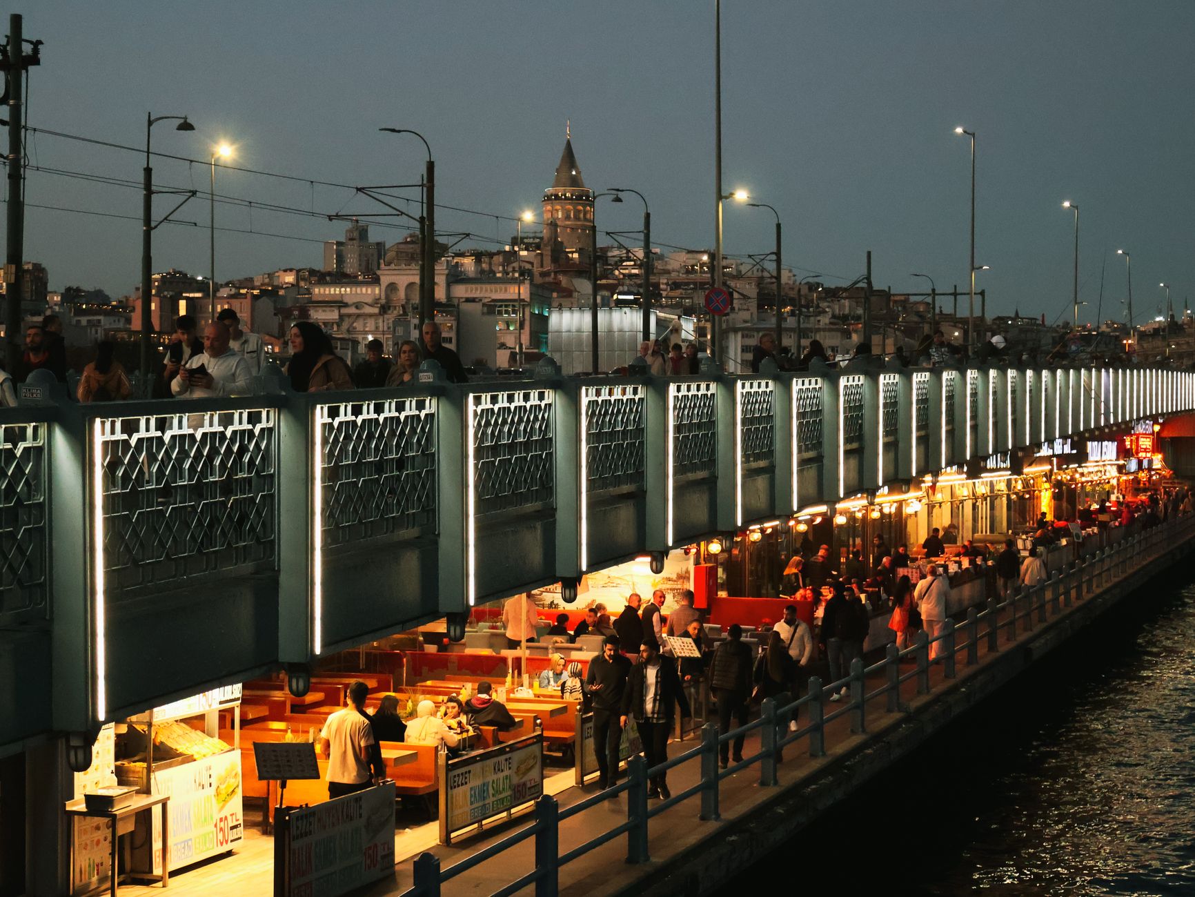 Night view of Galata Bridge bustling with people and distant Galata Tower in Istanbul. — Here is an important guide about cas