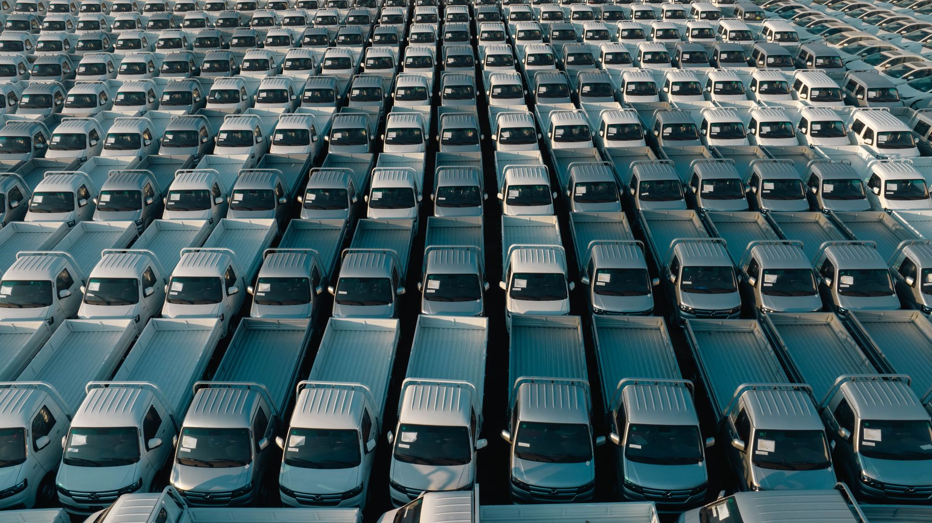 Overhead shot of a large collection of white pickup trucks parked in neat rows, emphasizing industrial scale. — How to Keep Y