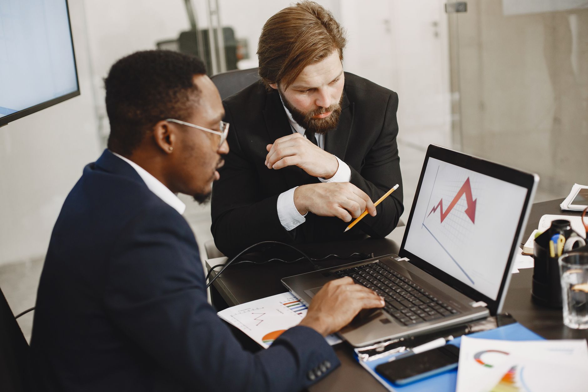 Two business professionals discuss marketing data on a laptop in a modern office. — How Traders Can Leverage Metatrader 4 on