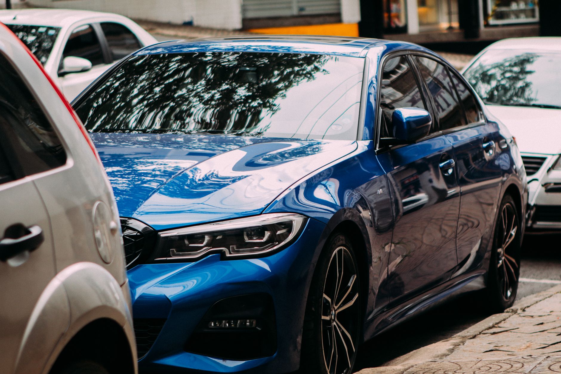 A vibrant blue luxury sedan parked on an urban street among cars. — Importance of Transmission Fluids