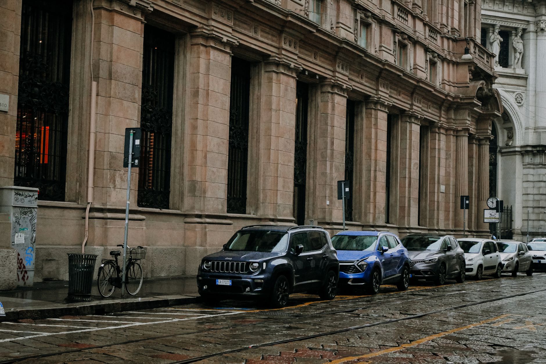 A rainy city street lined with parked cars and historic architecture, capturing an urban vibe. — It is very hard to have an i