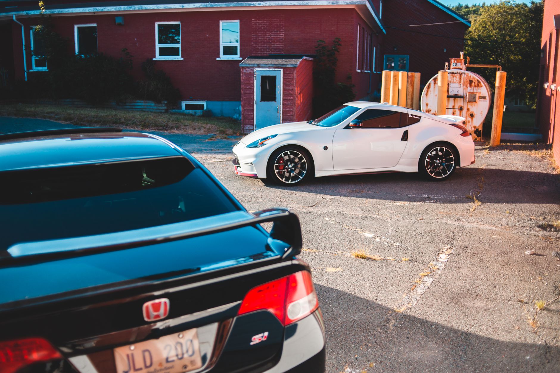 Expensive sports cars with glossy surface and spoilers parked on old uneven shabby pavement next to red simple constructions