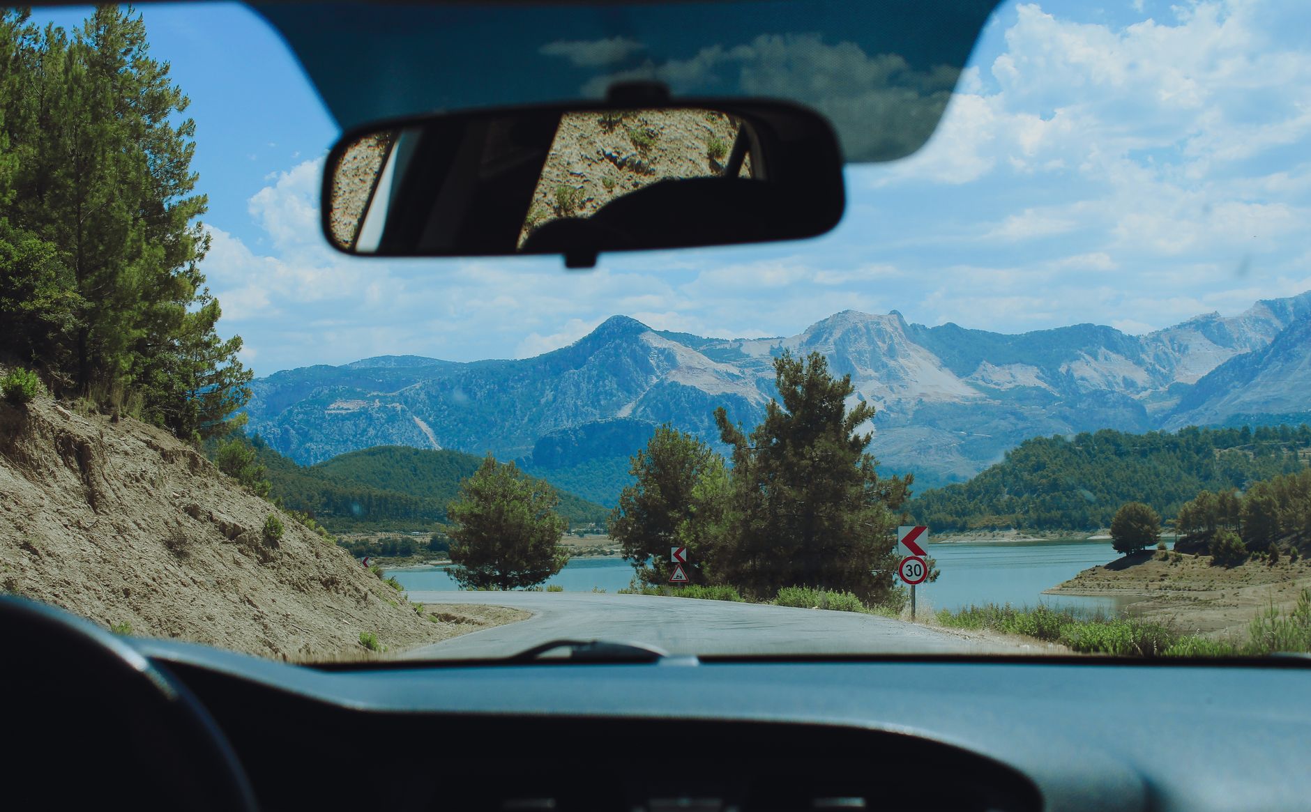 View from car interior of a winding road and mountain range with lush scenery, ideal for travel inspiration. — Practice These