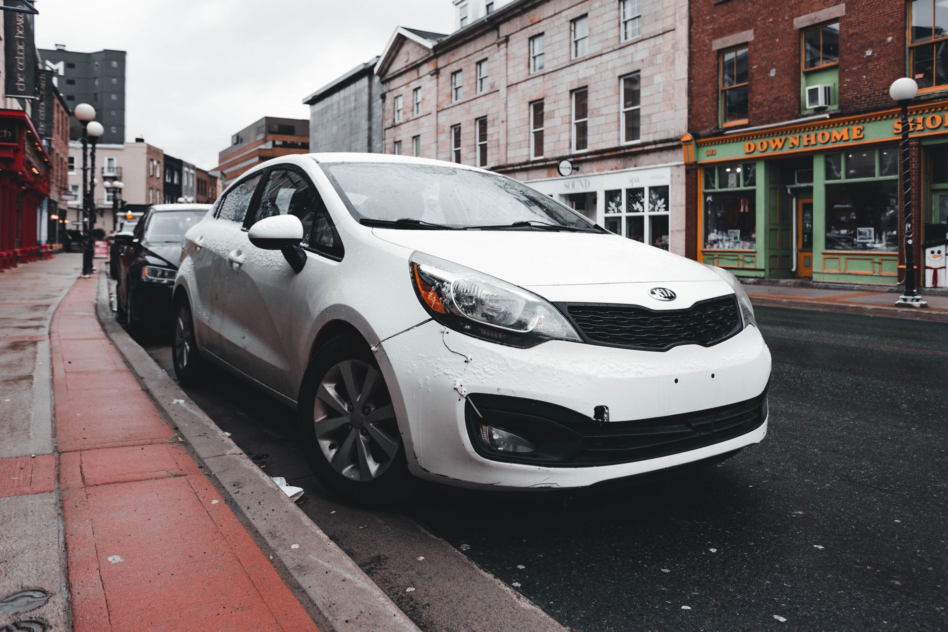 White Kia parked on a wet street with urban buildings in the background after rain. — Radiator Repair in New Orleans: When to