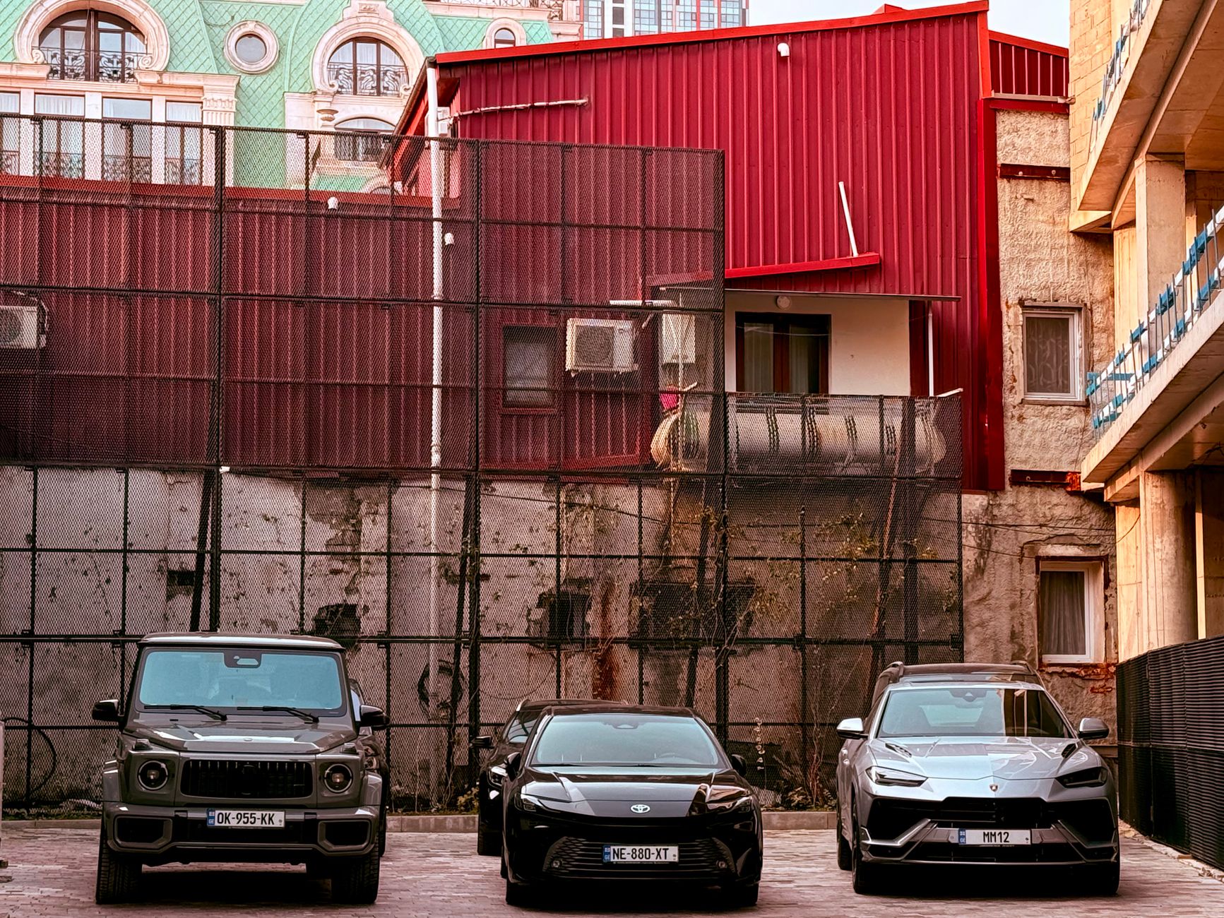 Three cars parked in an urban area with a red building and decorative architecture in the background. — Tips For Buying Tyres