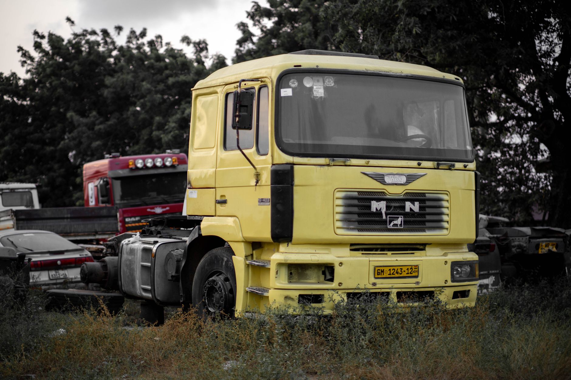 A yellow truck cab parked in an outdoor lot surrounded by other vehicles and trees. — Volvo Trucks - A Brief History of Volvo