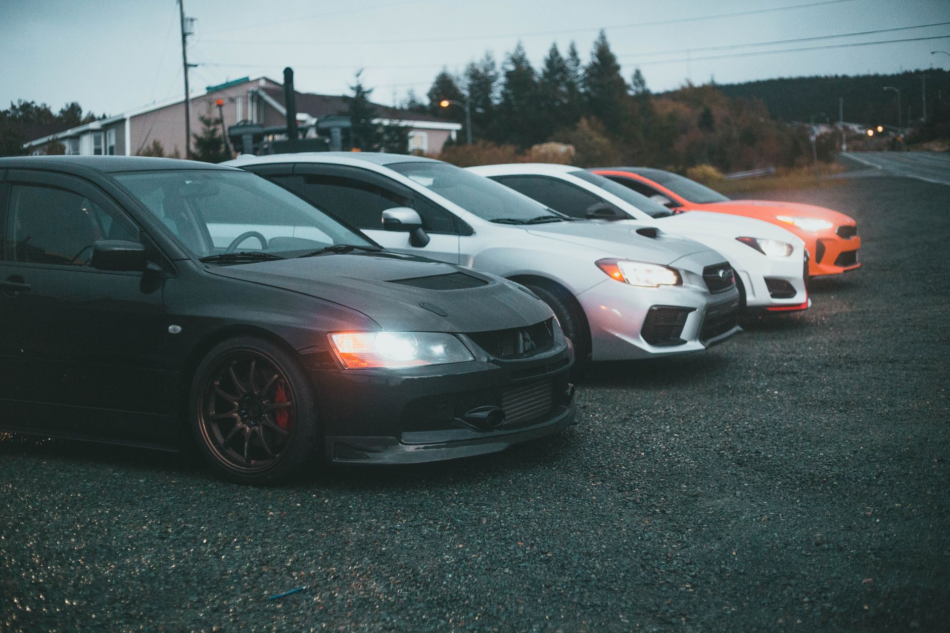 Four sporty cars parked on a rural roadside at twilight, showcasing modern automotive design. — Why You Should Rent Lamborghi